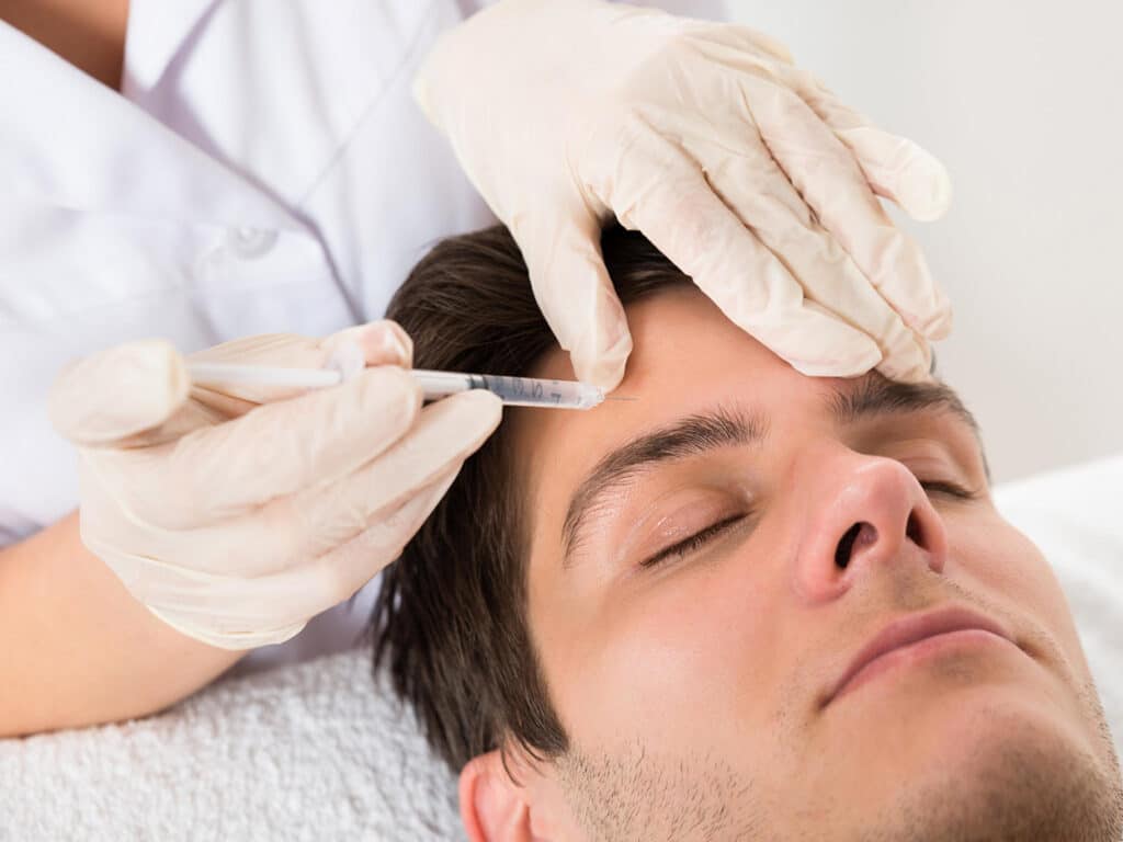 A man receiving a Juvederm filler injection to the forehead.