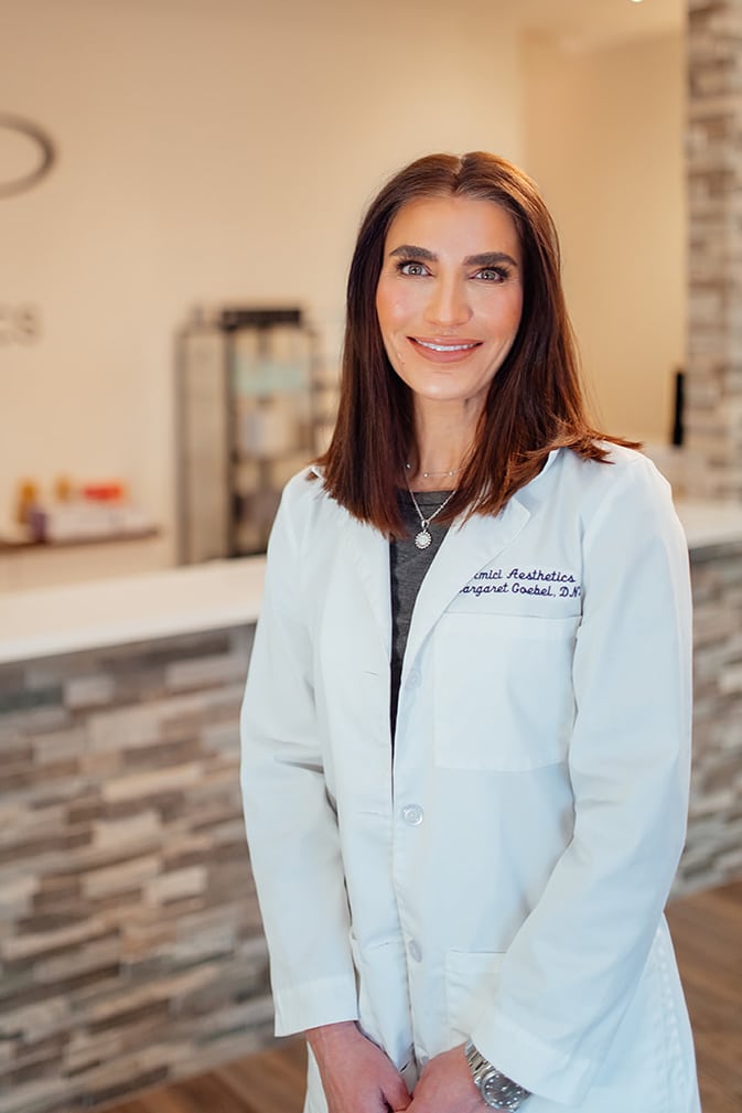 Margaret Goebel, NP - Owner of Amici Aesthetics Med Spa, standing in front of her office front desk.