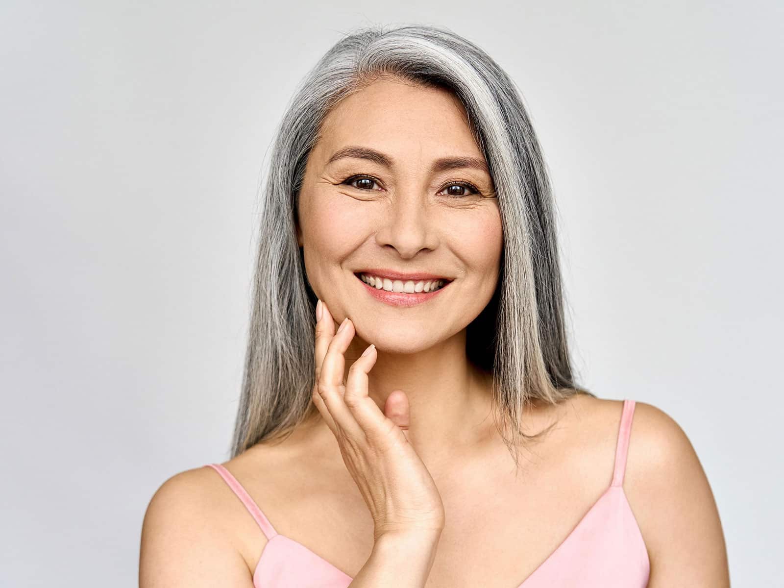 Beautiful middle aged woman smiles and touches her face where she received an Erbium Pixel Laser resurfacing treatment.